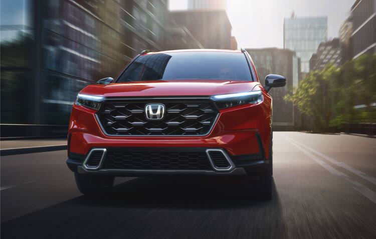 Straight front of 2025 CR-V Sport Touring in Radiant Red Metallic driving on downtown street.