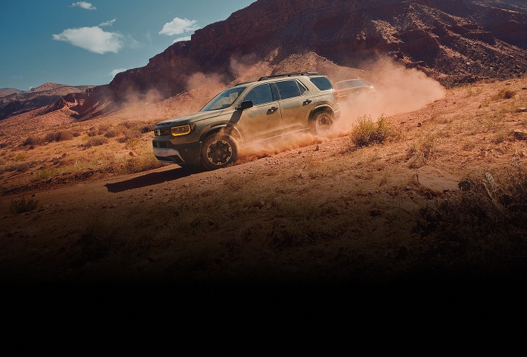 2027 Honda Passport TrailSport Elite in Ash Green Metallic profile driving on a dusty desert trail (Mid-Size SUV).